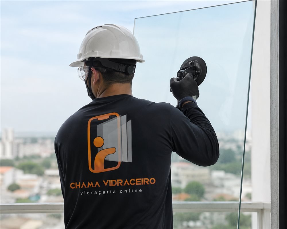 Vidraceiro de capacete e camiseta preta instalando painel de vidro com ventosas em uma sacada