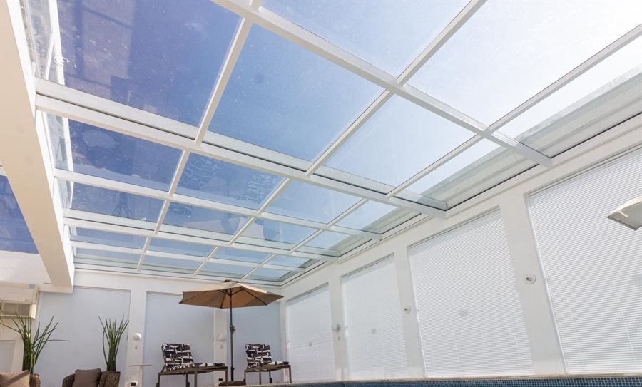 Cobertura de vidro com estrutura branca sobre área de piscina